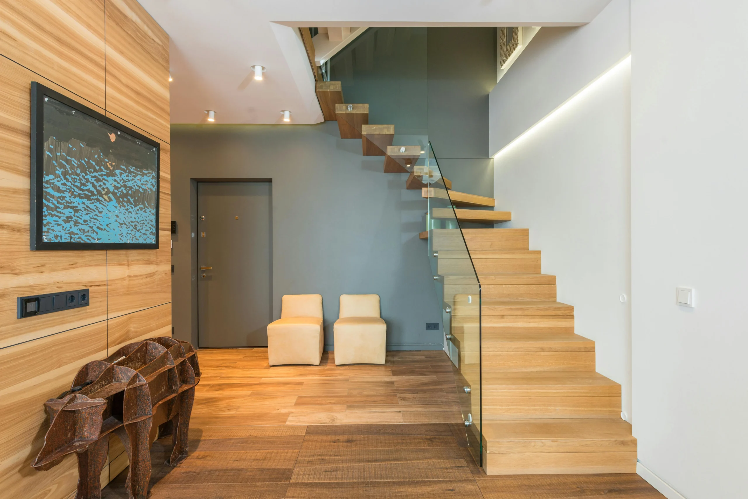 Escalera de Madera Clara con Baranda de Vidrio y Pared Gris