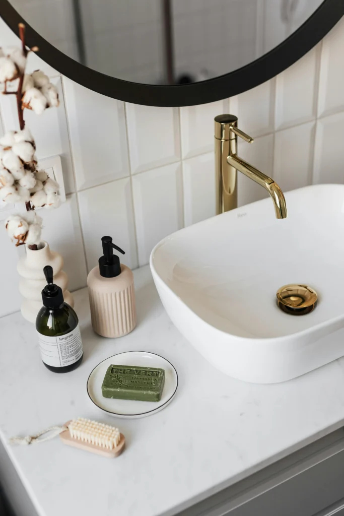 Baño contemporáneo con lavabo blanco, grifería dorada y espejo circular
