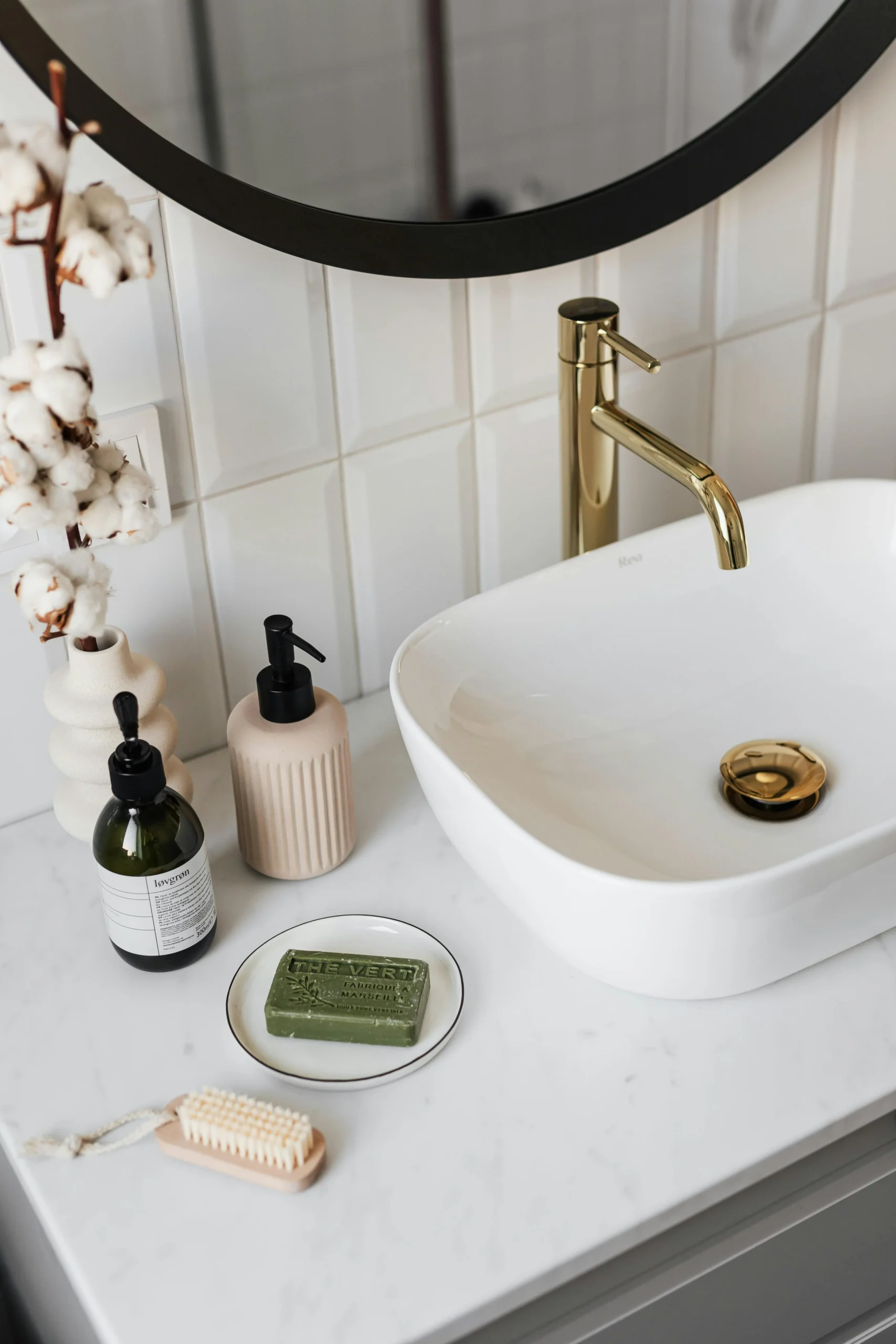 Baño contemporáneo con lavabo blanco, grifería dorada y espejo circular